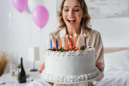 Birthday cake in hands of excited woman on blurred background in bedroomの写真素材