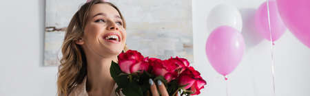 Happy woman holding roses near balloons at home, bannerの写真素材