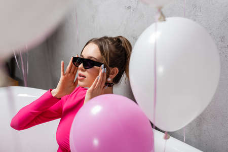 Young woman in sunglasses sitting in bathtub near blurred balloons on foregroundの写真素材