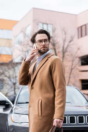 young man in glasses and coat talking on smartphone outsideの写真素材