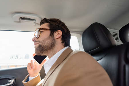 worried man in glasses and suit talking on smartphone in carの写真素材