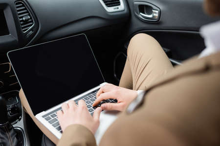 cropped view of businessman using laptop with blank screen in car