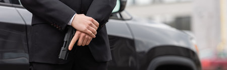cropped view of bodyguard in suit holding gun near modern auto, banner