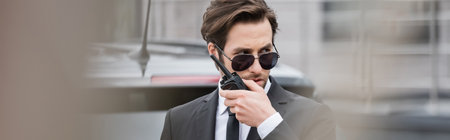 bodyguard in sunglasses and suit using walkie talkie outside, banner