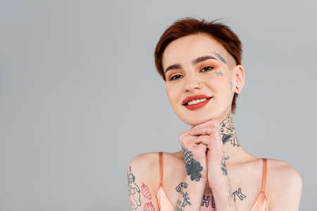tattooed young woman with red lips smiling isolated on grayの写真素材