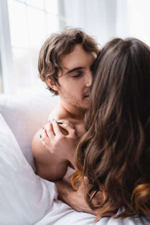 Young man kissing brunette girlfriend on bed
