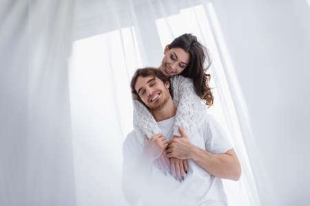 Young woman smiling while hugging boyfriend near window