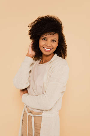 attractive african american woman adjusting hair isolated on beigeの写真素材