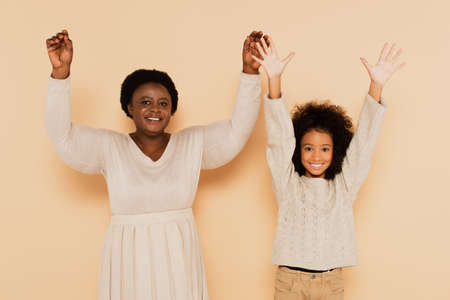 excited african american granddaughter and grandmother holding hands up on and showing palms on...