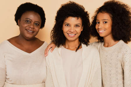 smiling african american grandmother, daughter, granddaughter looking at camera on beige backgroundの写真素材