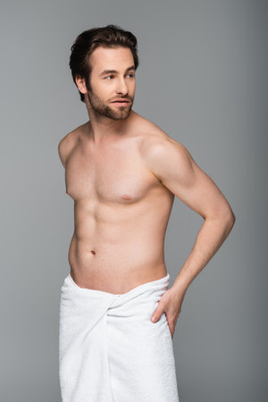young muscular man wrapped in white towel looking away isolated on grayの写真素材