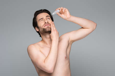 bearded man with closed eye applying eye drops isolated on gray