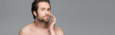 shirtless man applying face cream isolated on gray, bannerの写真素材
