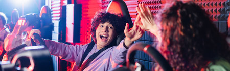 excited teenage friends giving high five while gaming on car simulators, banner