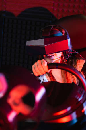 smiling girl in vr headset racing in car simulator on blurred foregroundの写真素材