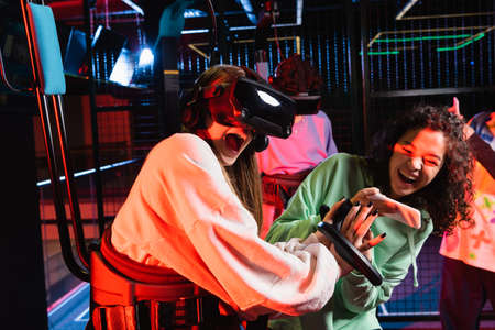 excited african american girl taking photo of astonished girl in vr headset