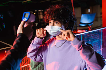 teenage gamer adjusting medical mask near controller with pyrometer
