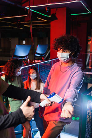 controller with pyrometer showing thumb up near gamer and friends in medical masks