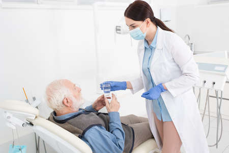dentist giving glass of water to senior patient lying in dental chairの写真素材