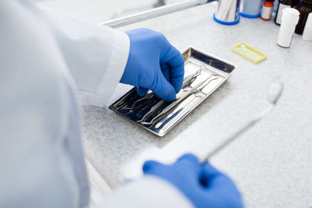 cropped view of dentist in latex gloves taking medical equipment from tray on medical tableの写真素材