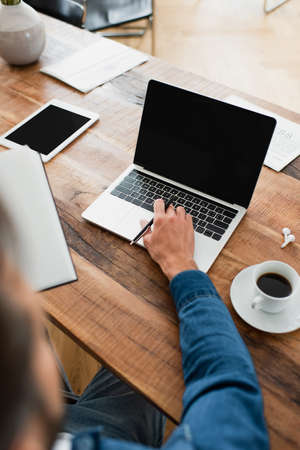 partial view of freelancer working at laptop near digital tablet and cup of coffee