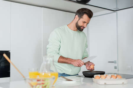 man preparing breakfast from chicken eggs near orange juice on blurred foreground