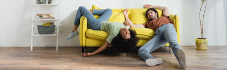 exhausted young multiethnic couple lying on yellow sofa and suffering from heat in summer, banner