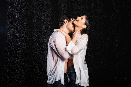 romantic boyfriend embracing with sexy girlfriend in wet clothes in rain drops on black backgroundの写真素材
