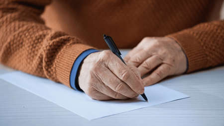close up view of male elderly hands writing on empty blank with penの写真素材