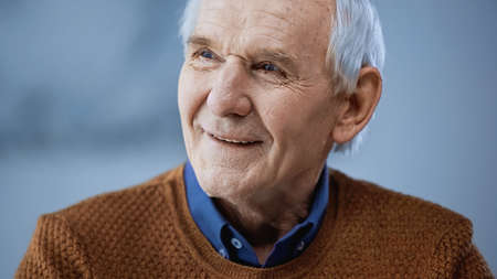 portrait of cheerful elderly man looking away on gray backgroundの写真素材