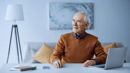 elderly man sitting at table with laptop and smartphone at homeの写真素材