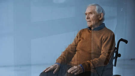 thoughtful senior man in wheelchair looking away on gray background