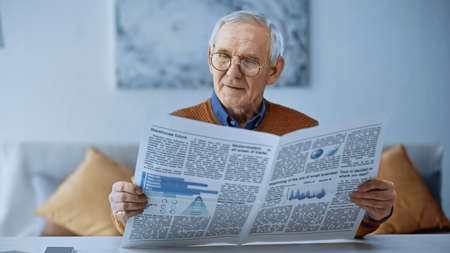 elderly man in glasses reading newspaper at modern living roomの写真素材