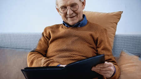 happy elderly man sitting on sofa with family album in living roomの写真素材