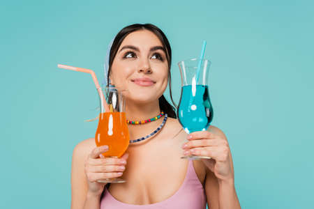 Smiling woman in necklaces holding cocktails isolated on blueの写真素材