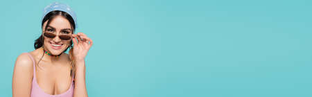 Pretty woman in bandana holding sunglasses isolated on blue, bannerの写真素材