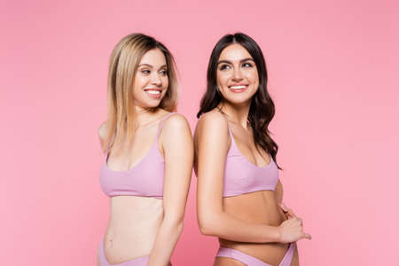 Smiling woman looking at brunette friend in swimwear isolated on pinkの写真素材