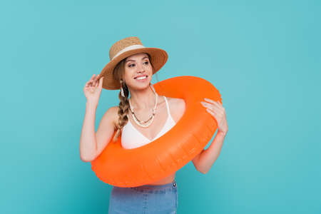 Smiling woman in straw hat holding swim ring isolated on blueの写真素材