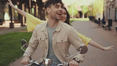 excited man and happy woman with outstretched hands riding motorcycle on streetの写真素材