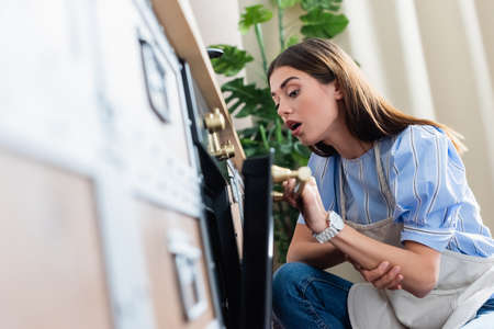 interested young adult woman in apron looking into oven with open mouth in modern kitchenの写真素材
