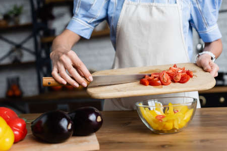 partial view of young adult woman putting sliced cherry tomatoes into vegetables salad in modern kitchenの写真素材