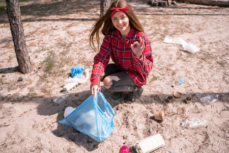 happy woman showing ok sign near trash bag and rubbish on groundの写真素材