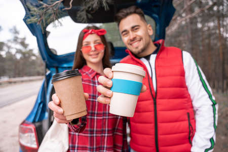 blurred man and woman holding reusable and paper cups near car