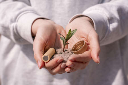 cropped view of woman holding battery, plastic cap and green plant in handsの写真素材