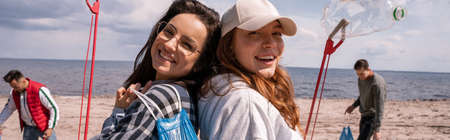 happy young women with grabbers and trash bags outside, banner