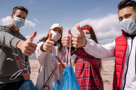 young volunteers in medical masks holding trash bags and grabbers while showing thumbs up, pick up trash conceptの写真素材