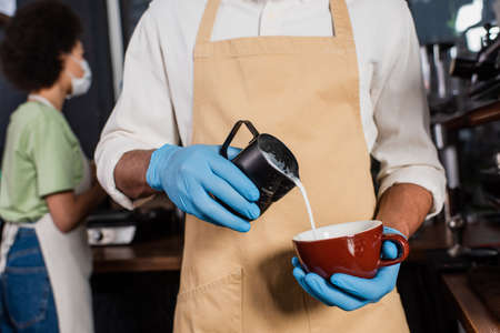 African american barista in latex gloves making coffee with milk in cafeの写真素材