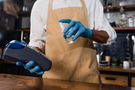 Cropped view of payment terminal and antiseptic in hands of african american barista in latex glovesの写真素材