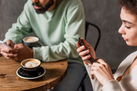African american woman using cellphone near blurred coffee and boyfriend in cafeの写真素材