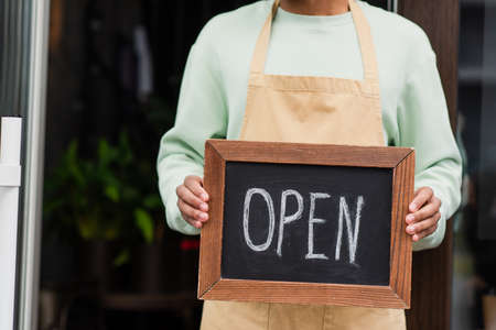 Cropped view of african american barista holding chalkboard with open lettering near cafe